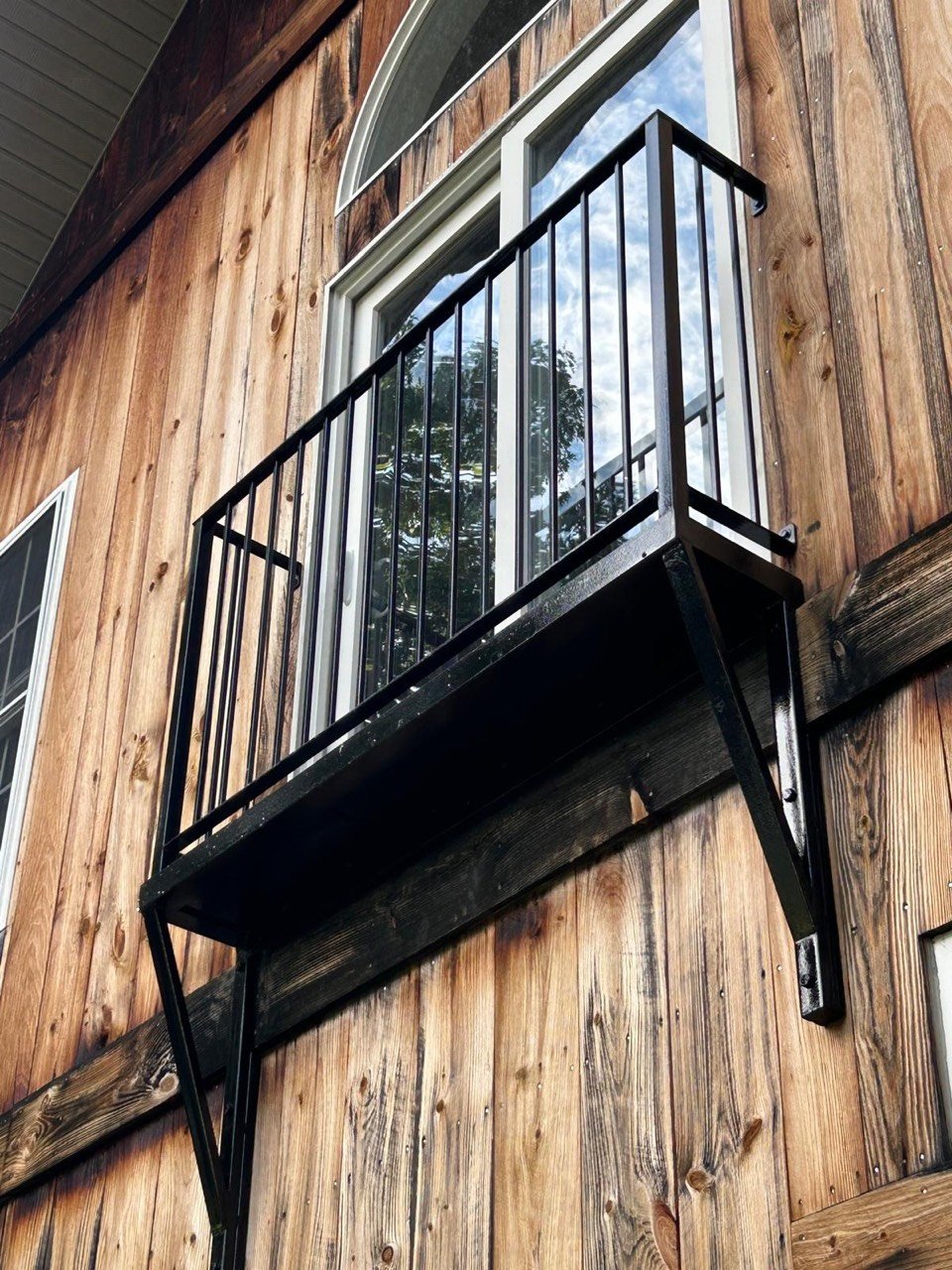 Black steel balcony railing on a wood-sided building