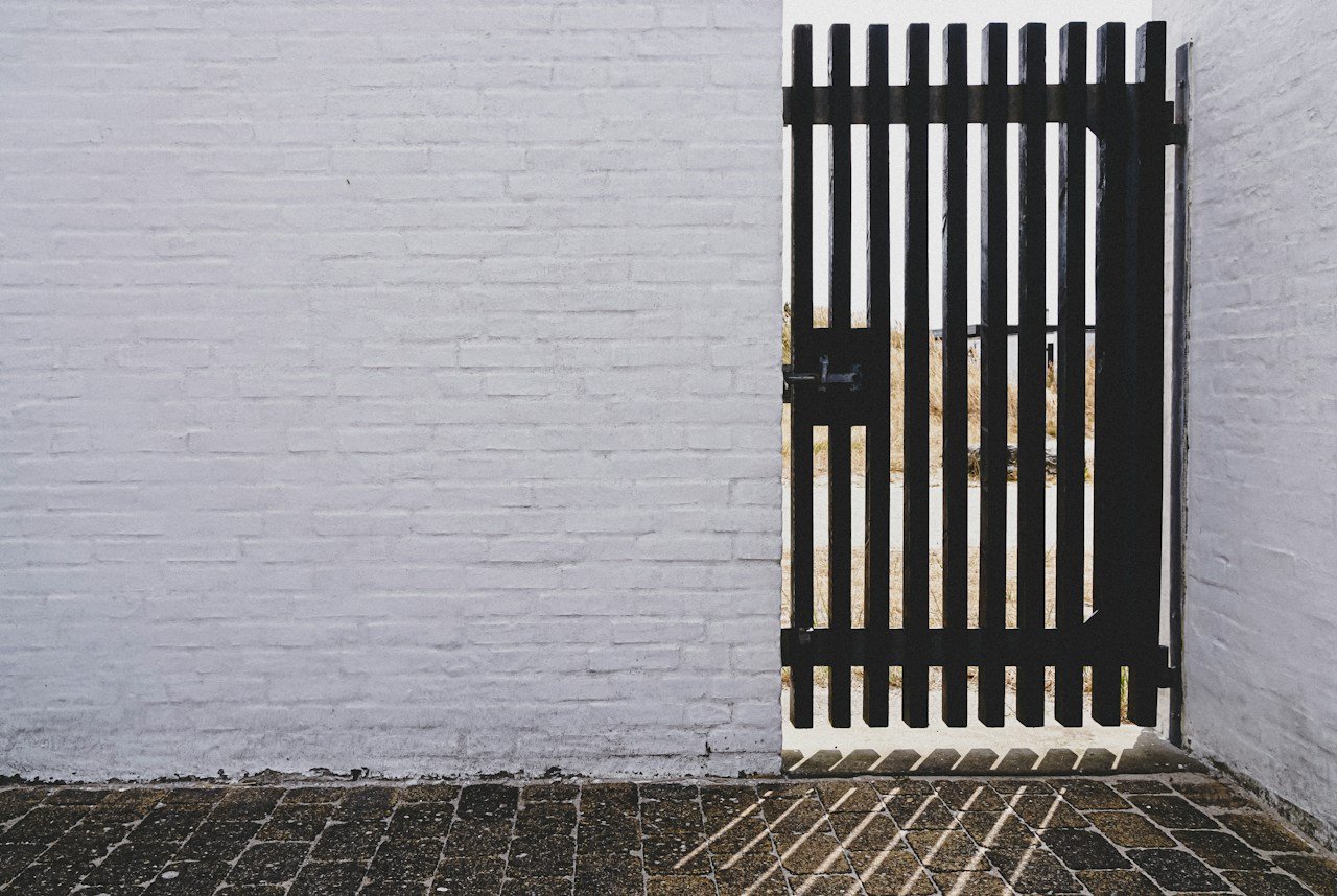Black steel gate with a latch set into a white brick wall
